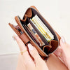 A hand holds a brown leather wallet with a zipper, showing several cards inside for RFID protection.