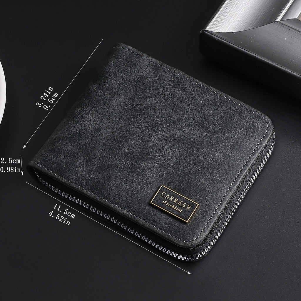 A black leather zipper wallet with a gold engraved nameplate shown on a dark surface.