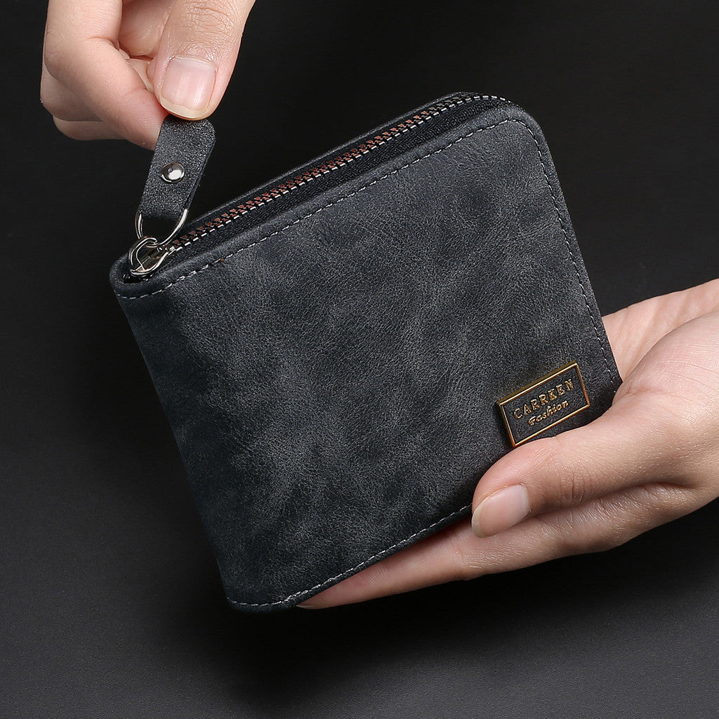 A dark gray leather zipper wallet is held in a hand, showing the texture and engraved brand name.